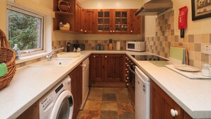 Una cocina compacta con armarios de madera, microondas, lavavajillas y ventana con vistas a zonas verdes.