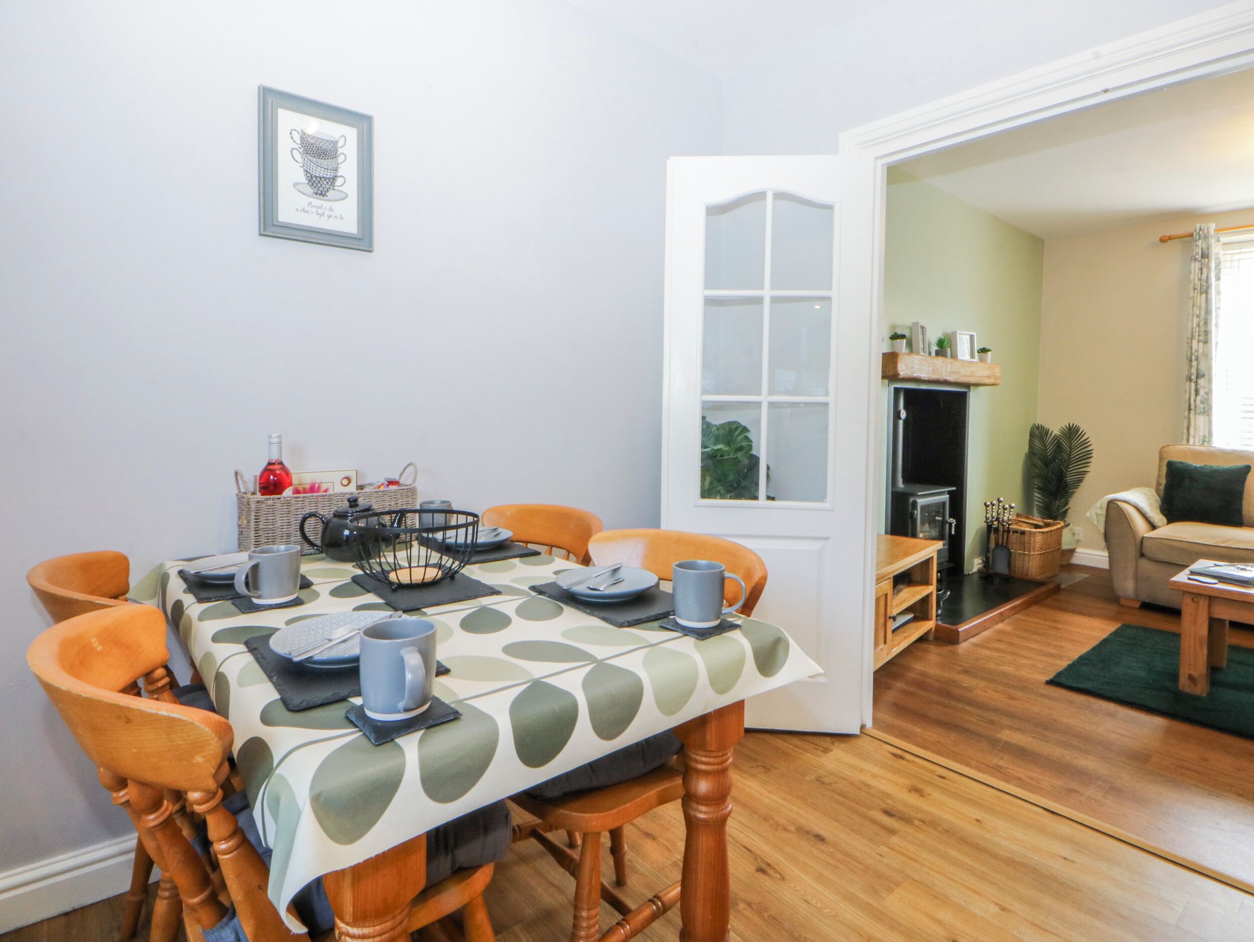 A dining area with a table set for four, chairs, a basket with items, and a framed picture on the wall.