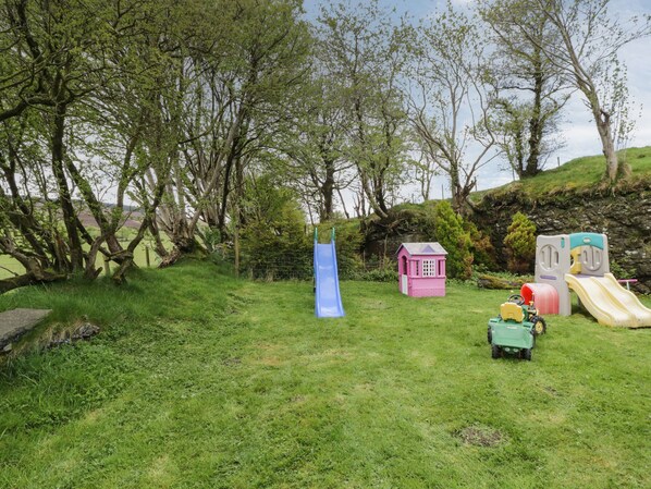 A grassy outdoor area with a blue slide, a pink playhouse, and a green toy tractor. - Glan Gors (Denbigh)