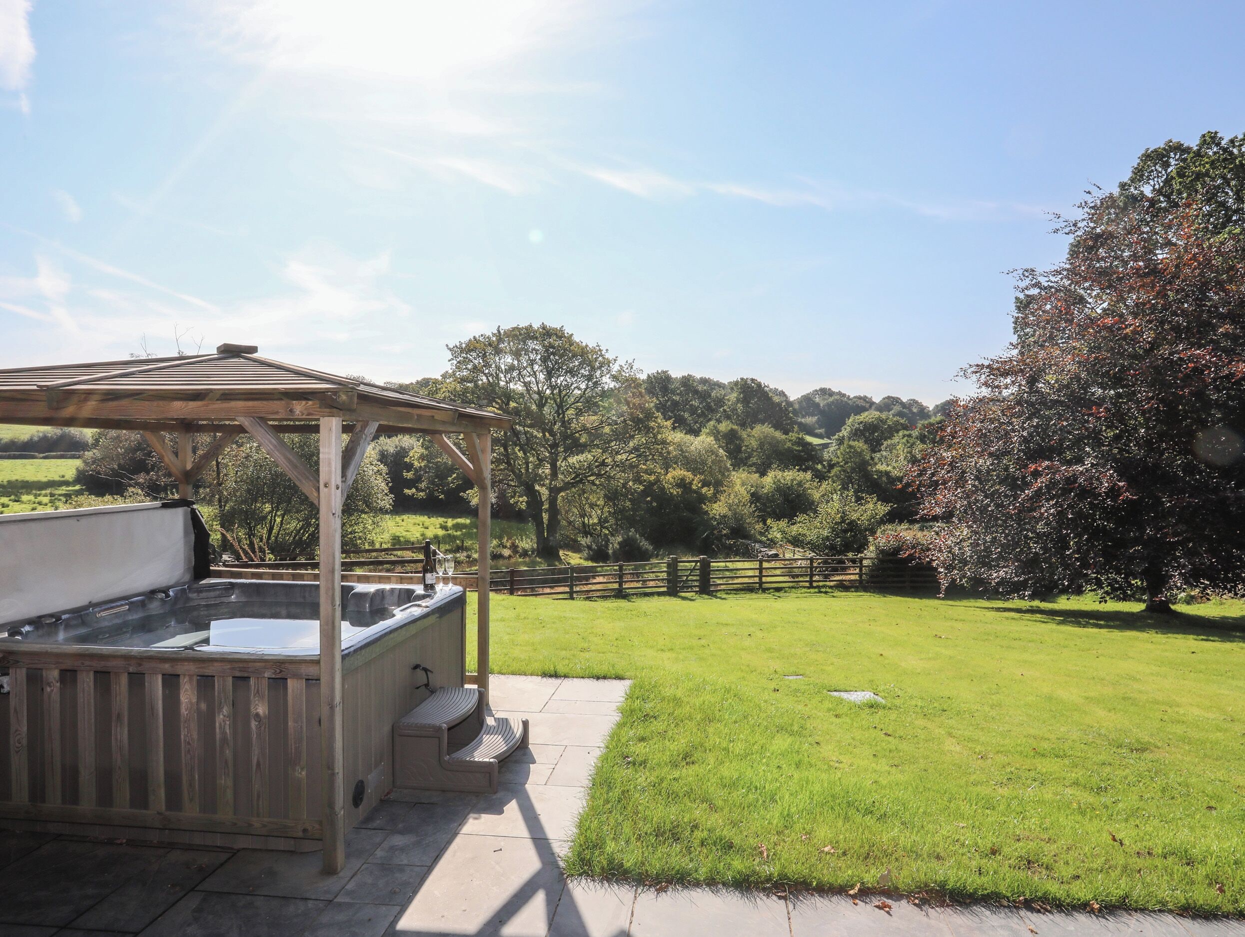 A wooden gazebo with a built-in hot tub and a stone patio.