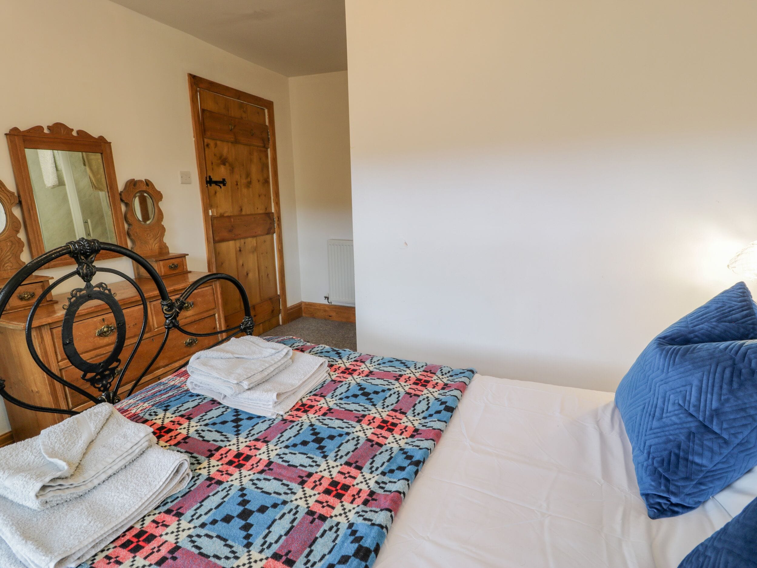 A bedroom with a bed, a wooden door, a dresser with a mirror, and a patterned blanket.