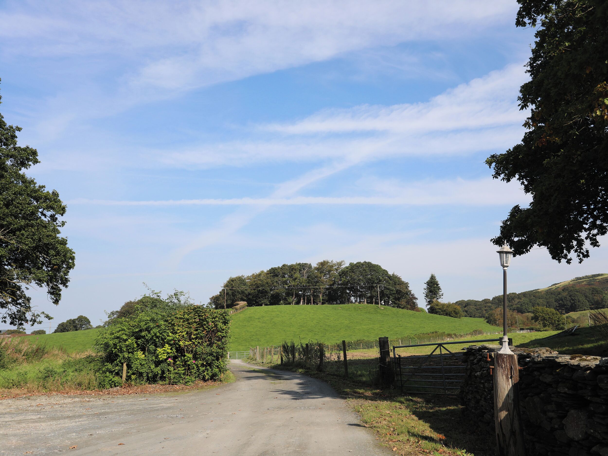 Un chemin de campagne menant à une colline, avec une clôture et un lampadaire.