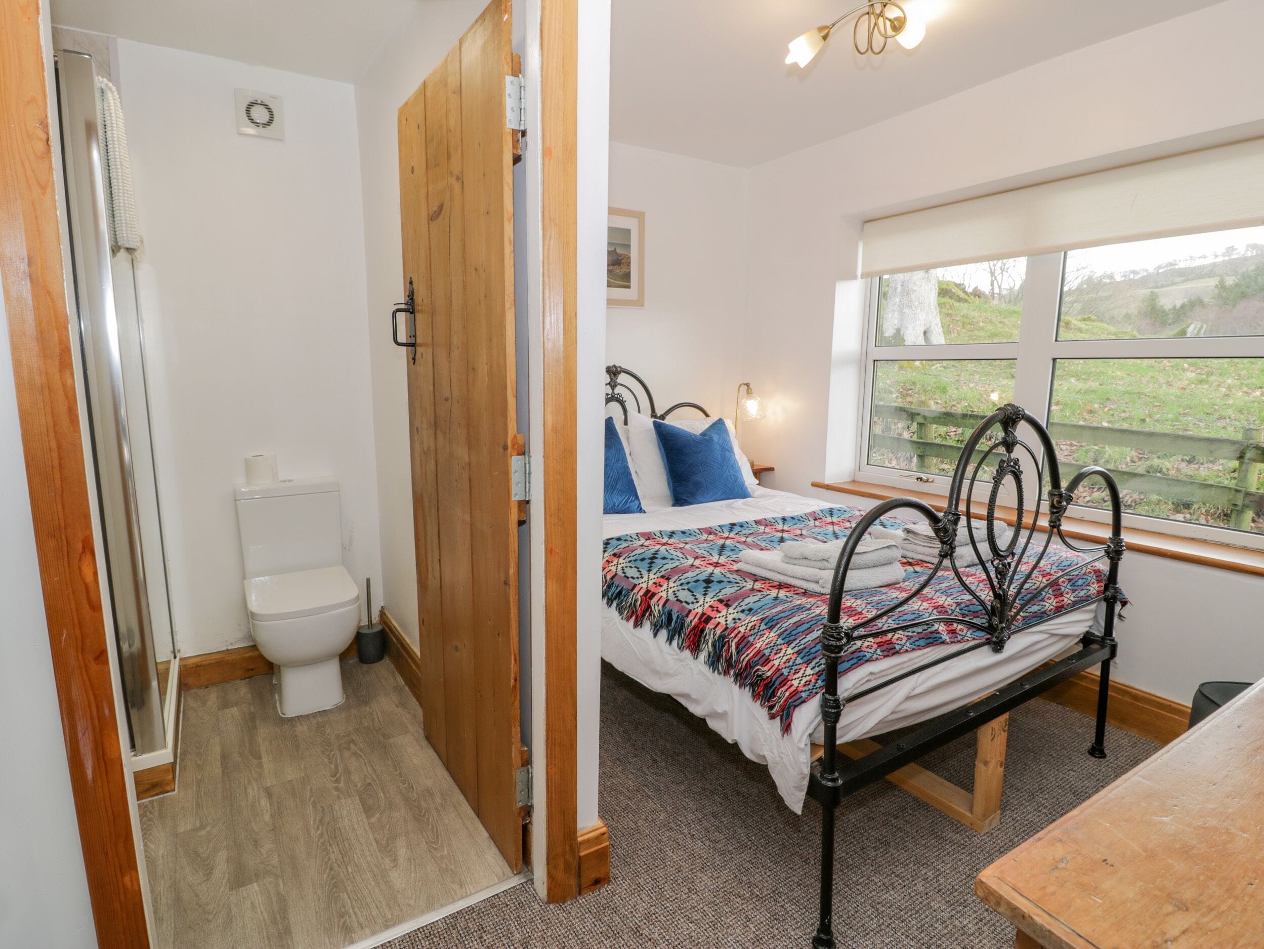 A bedroom with a bed, a window with a view, a wooden door, and a toilet.