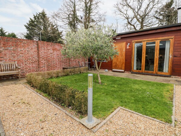 A brick wall, a wooden bench, a small tree, a gravel path, and a building with large glass doors. - Rabbit's Warren (Fareham)