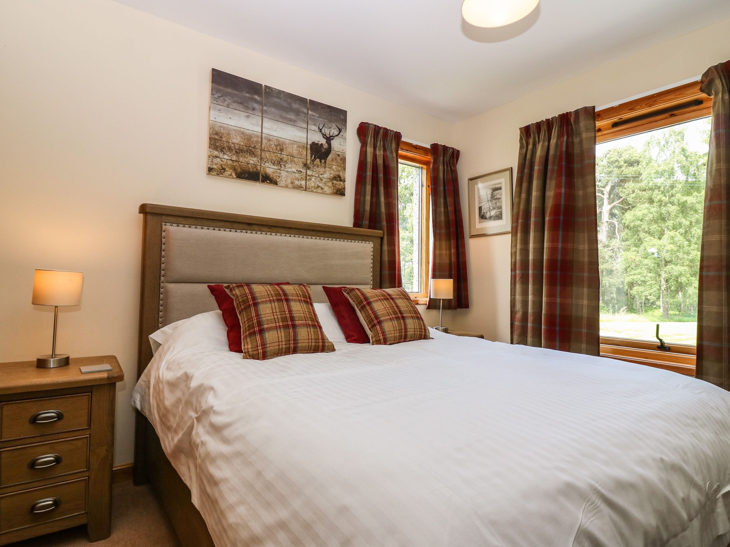 A neatly made bed with plaid pillows, a wooden headboard, and a framed picture above it.