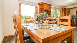 A dining area with a wooden table set for four, surrounded by chairs. There is a vase with flowers on the table, and a window with a view of greenery outside. - Birchbank (Grantown-on-Spey)