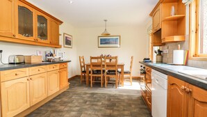 A kitchen with wooden cabinets, a dining table with chairs, and a tiled floor. - Birchbank (Grantown-on-Spey)