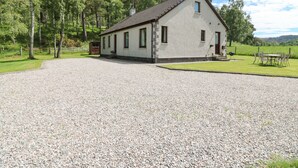 A white building with a tiled roof, surrounded by gravel, trees, and a grassy area. - Birchbank (Grantown-on-Spey)