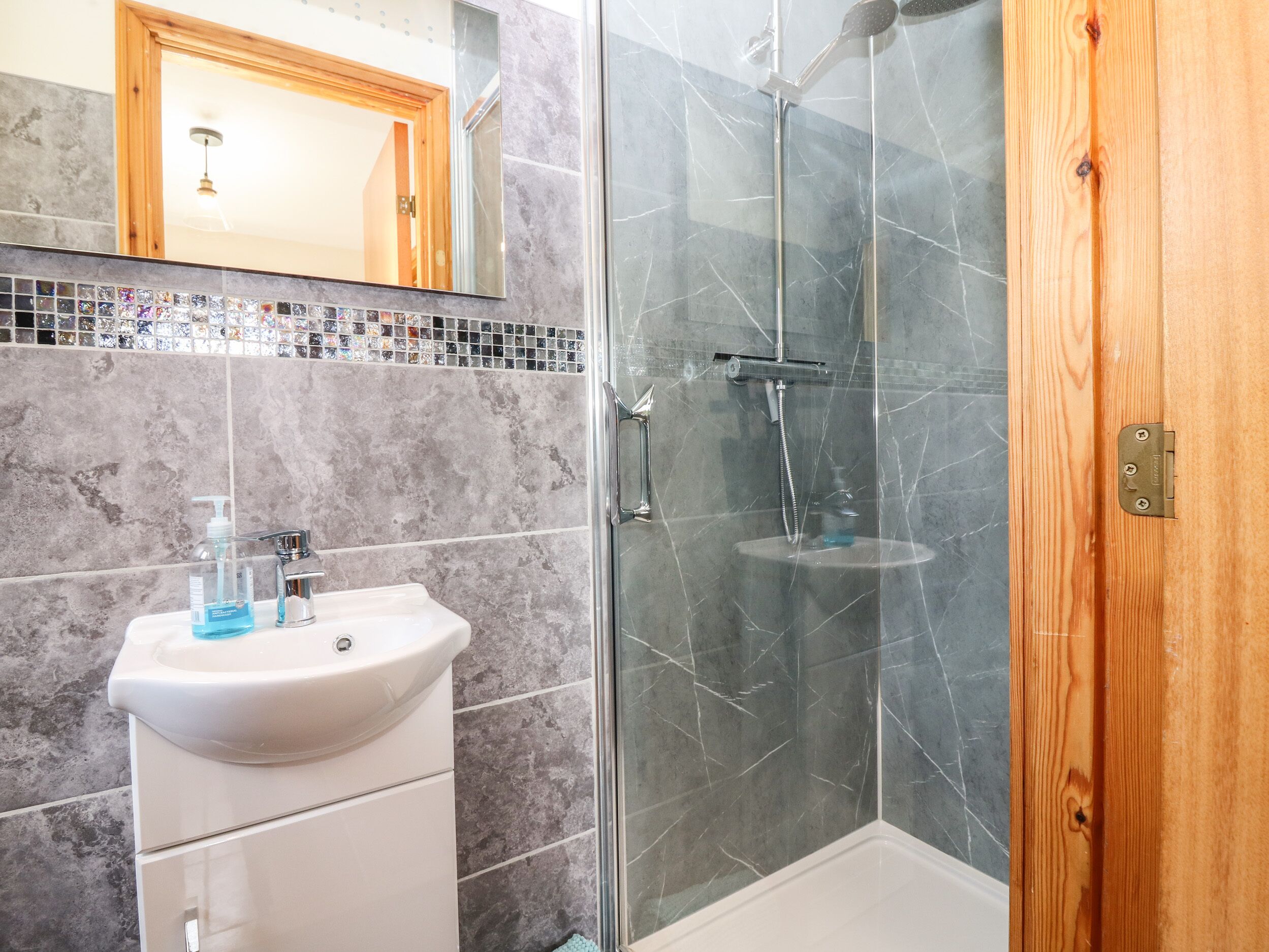 Un baño con un lavabo blanco, una ducha con puerta de vidrio y una puerta de madera.
