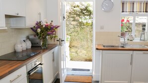 A kitchen with white cabinets, a wooden countertop, a built-in oven, a sink, and a clock on the wall. - Coachmans Cottage (Grange-over-Sands)