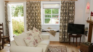 A cozy living room with a sofa, a television, and a window with curtains. - Coachmans Cottage (Grange-over-Sands)
