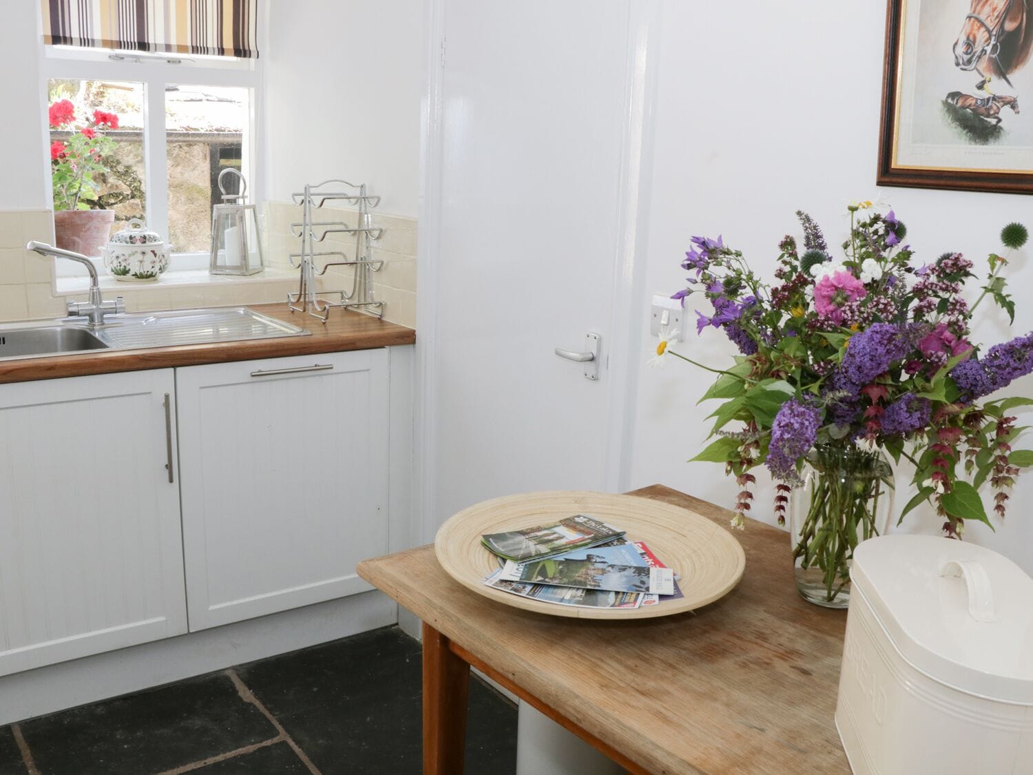 A kitchen with white cabinets, a wooden countertop, a sink, and a vase of purple flowers.