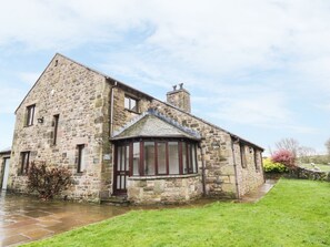 Traditional stone house with a gabled roof and bay window, featuring a stone chimney and porch area.
