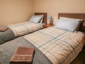 Two single beds with matching headboards and plaid-patterned bedspreads, each accompanied by a bedside table with a lamp and a folded towel.
