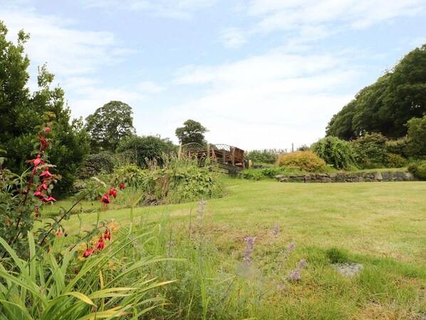 A garden with a wooden deck, various plants, and a stone wall. - Hen Ysgubor Cottage (Bala)