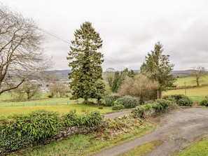 Surrounded by a serene rural landscape, this property offers a peaceful escape with a dirt road leading through a field, lined by a stone wall and a wooden bench.