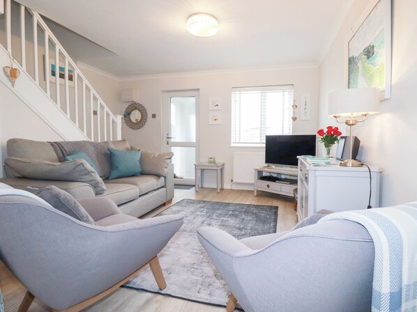 A living room with a sofa, two armchairs, a TV, and a small table with a lamp. - Gull Cottage (Padstow)