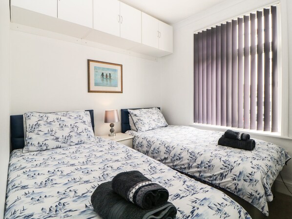 A hotel room with two beds, a framed picture on the wall, and a window with blinds.