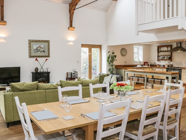 A spacious living area with a dining table set for four, a green sofa, and a kitchen in the background. - The Old Temperance Hall (Stoke-on-Trent)