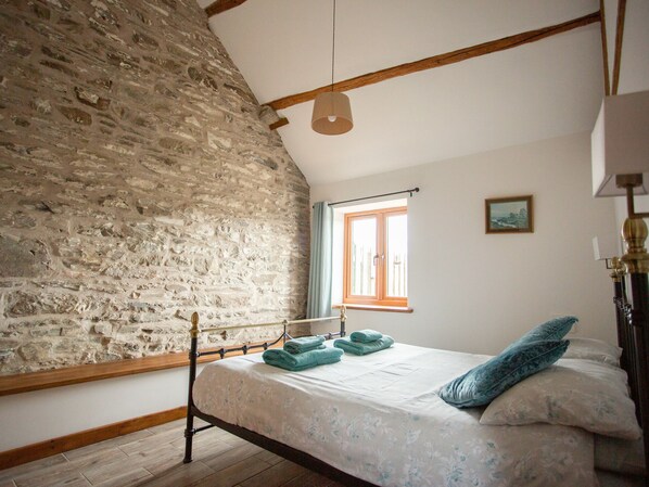 Ein Schlafzimmer mit Stehwänden, einem hölzernen Bettgestell, einem Fenster mit Vorhängen und einer Nachttischlampe.