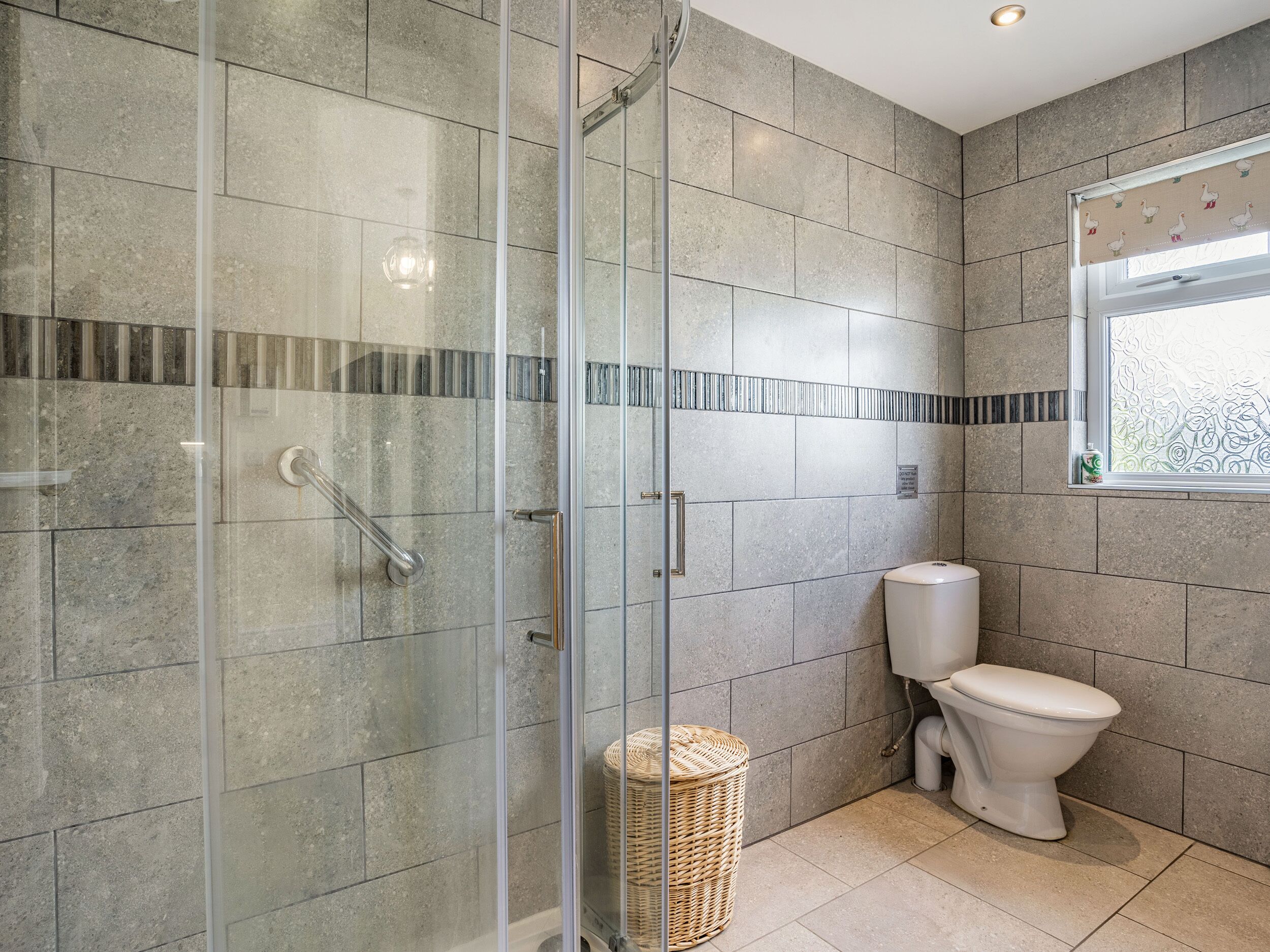 A modern bathroom with a glass shower enclosure, a toilet, and a window with a decorative pattern.