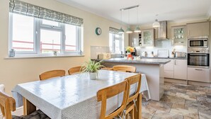 A modern kitchen with a dining area, featuring a central island, pendant lighting, and a view of the outside. - Yr Hen Ffald (Swansea)