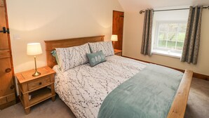 A bedroom with a wooden bed, two bedside tables, a window with curtains, and a hanging light fixture. - Llwyn Celyn (Dolgellau)