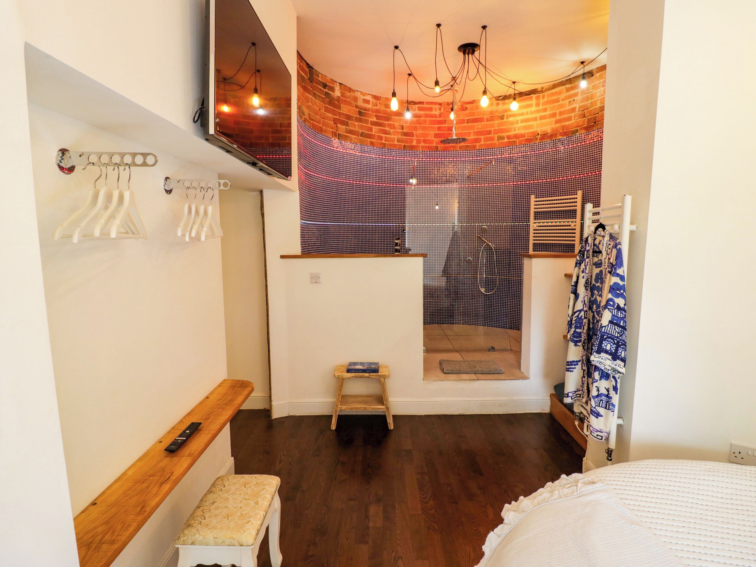 A modern bathroom with a shower, wooden bench, towel rack, and a hanging robe.