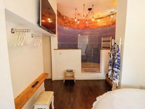 A modern bathroom with a shower, wooden bench, towel rack, and a hanging robe. - Lower Tundridge Cottage (Worcester)