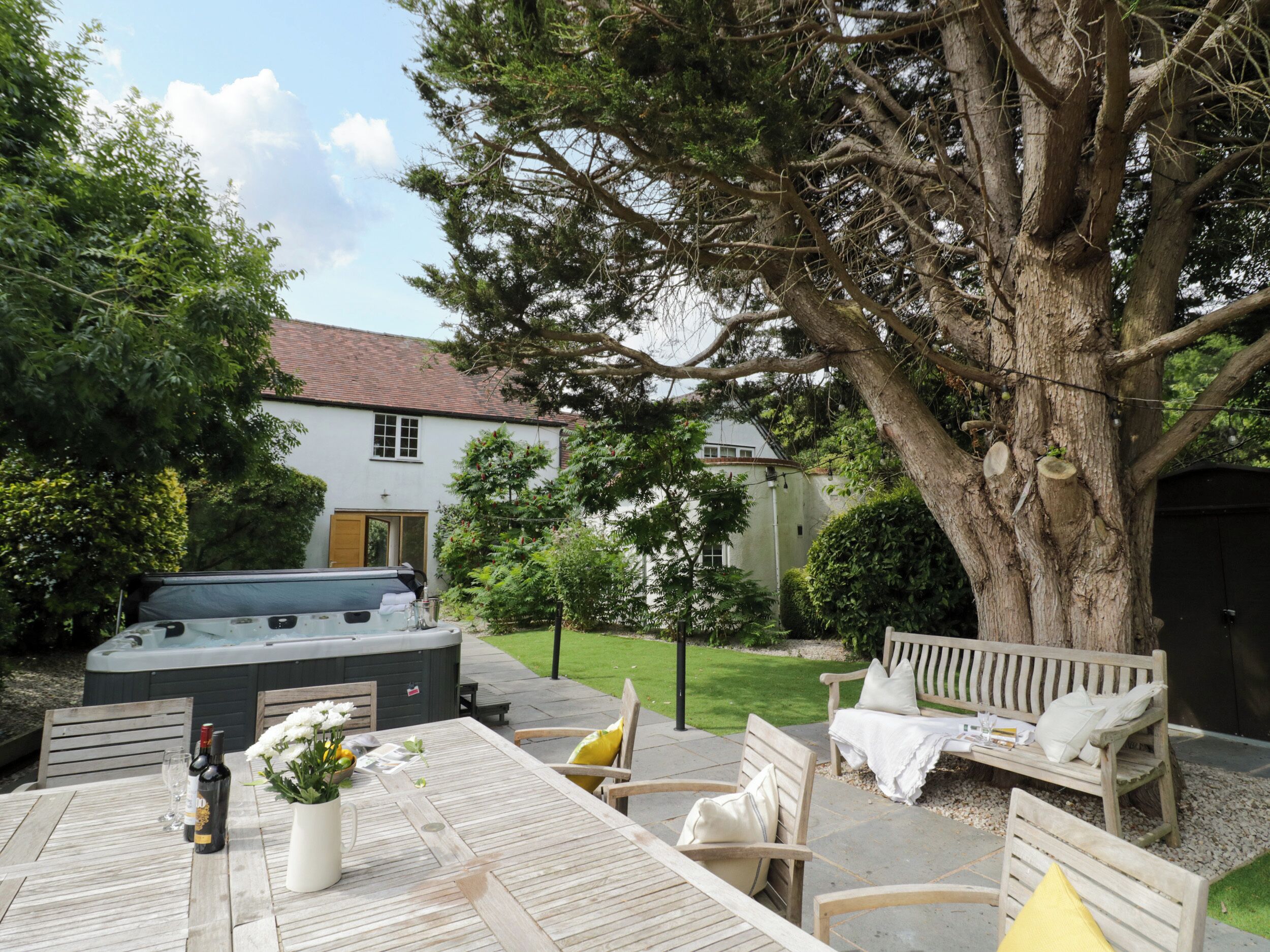 A wooden deck with a hot tub, outdoor seating, and a large tree.
