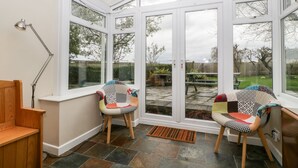 A conservatory with two chairs, a wooden bench, and a table.