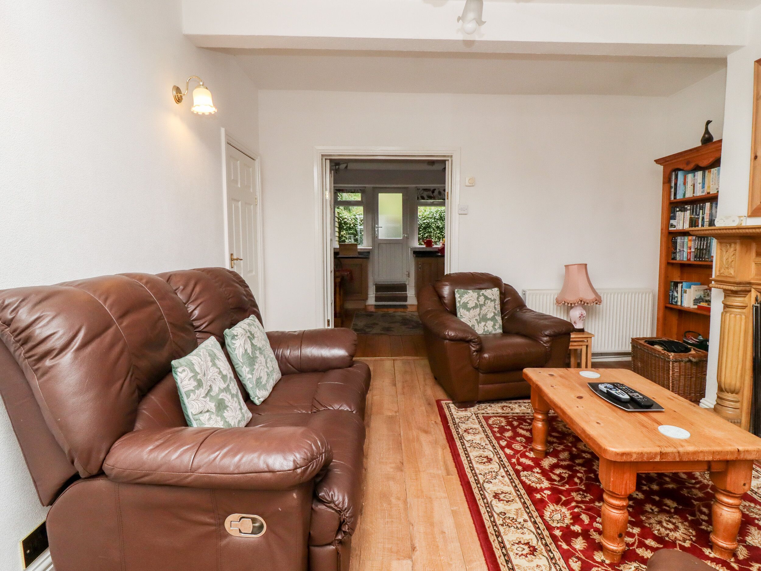A living room with a brown leather sofa, a matching armchair, a wooden coffee table, and a bookshelf.