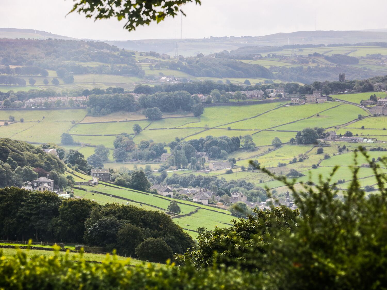 A rural landscape with rolling green fields, scattered houses, and a prominent tower structure.