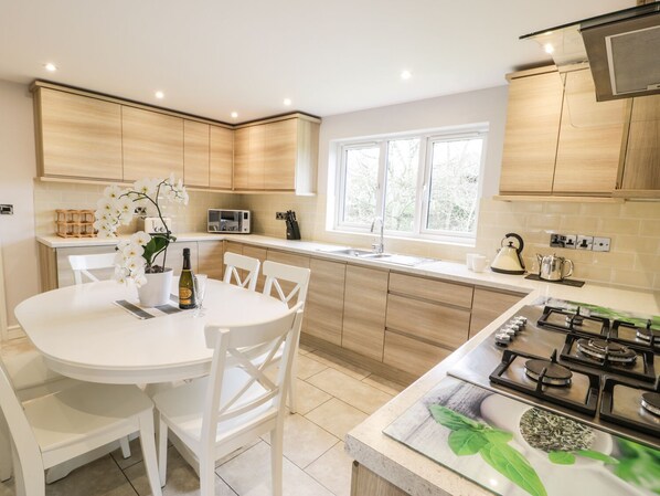 A modern kitchen with white cabinetry, a dining table with chairs, a gas stove, a microwave, and a window providing natural light.
