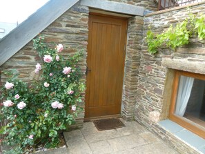 Stunning stone facade with a charming entrance, featuring a small window and a beautiful garden with roses.