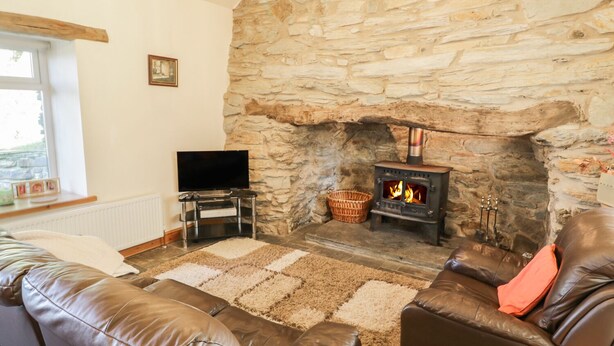 A cozy living room with a stone fireplace, leather sofas, a flat-screen TV, and a chandelier.