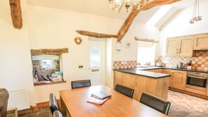 A cozy dining area with a wooden table and chairs, a kitchen with wooden cabinets, and a stone floor.