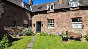 A stone building with a green door, windows, and a bench in the yard. - Gamekeepers Cottage (Alnwick)