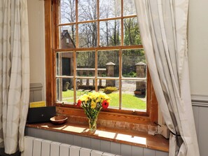 A window with a view of a garden, a wooden ledge, and a vase with flowers. - Gamekeepers Cottage (Alnwick)