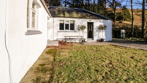A white single-story house with a front porch, a bench, and two potted plants. - White Hillocks Cottage (Kirriemuir)