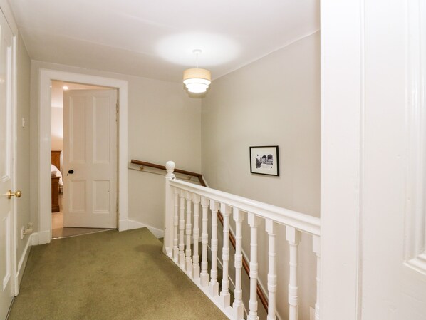 A hallway with a carpeted floor, white walls, a wooden railing, and a ceiling light fixture. - White Hillocks Farm House (Kirriemuir)