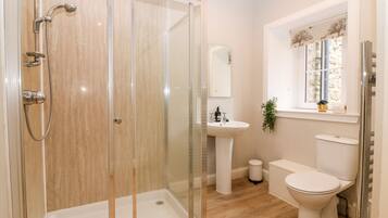 Een moderne badkamer met een douchecabine van glas, een wastafel op een voetstuk, een toilet en een raam met een plant.