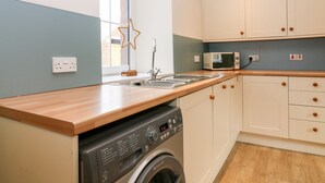 A compact kitchen with a washing machine, a microwave, and a sink. - White Hillocks Farm House (Kirriemuir)