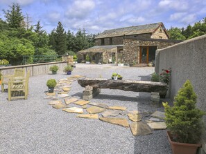 A stone building with a gravel courtyard, potted plants, and a wooden bench. - Knott Lodge (Sedbergh)