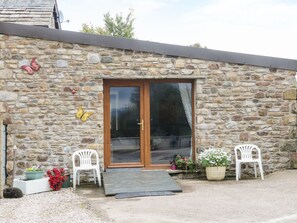 A stone building with a wooden door and glass panels, two white plastic chairs, and potted plants. - Knott Lodge (Sedbergh)