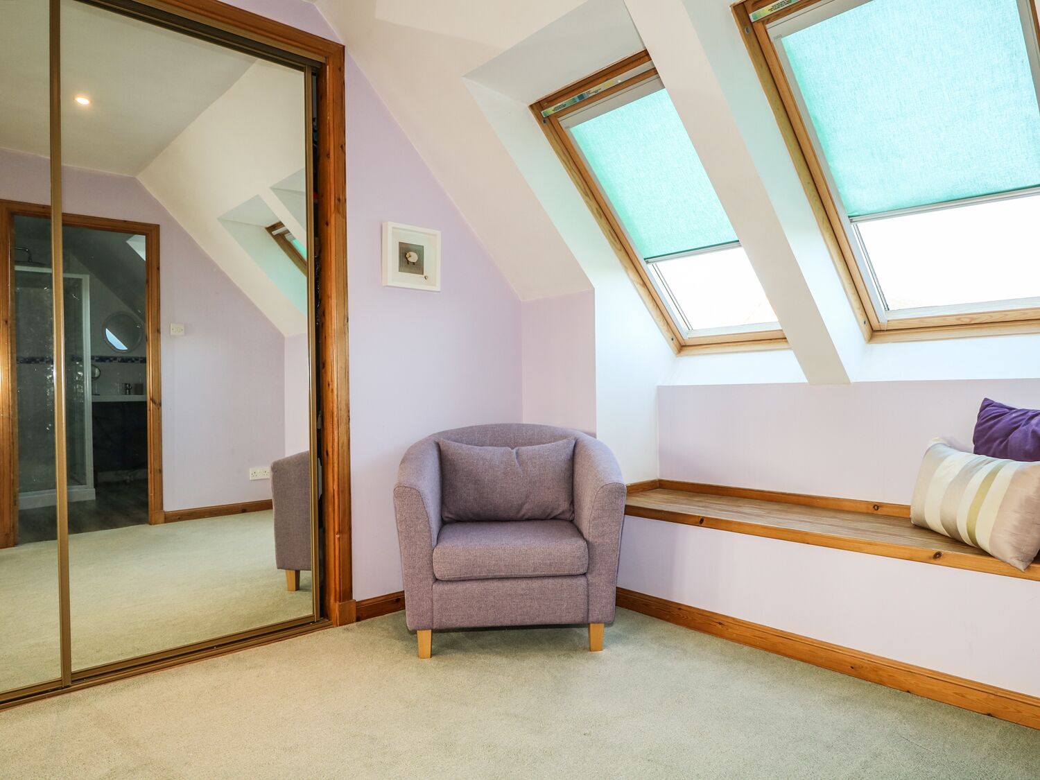 A room with a sloped ceiling, skylights, a cushioned bench, and a corner chair.