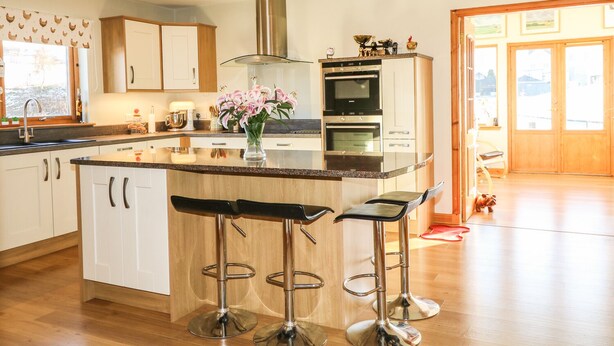 A modern kitchen with a central island, bar stools, stainless steel appliances, and a large window. - Corriemhor Beag (Grantown-on-Spey)
