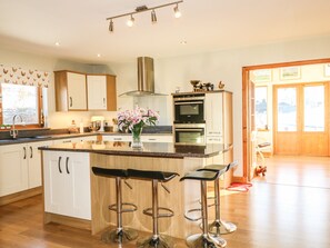 A modern kitchen with a central island, bar stools, stainless steel appliances, and a large window. - Corriemhor Beag (Grantown-on-Spey)