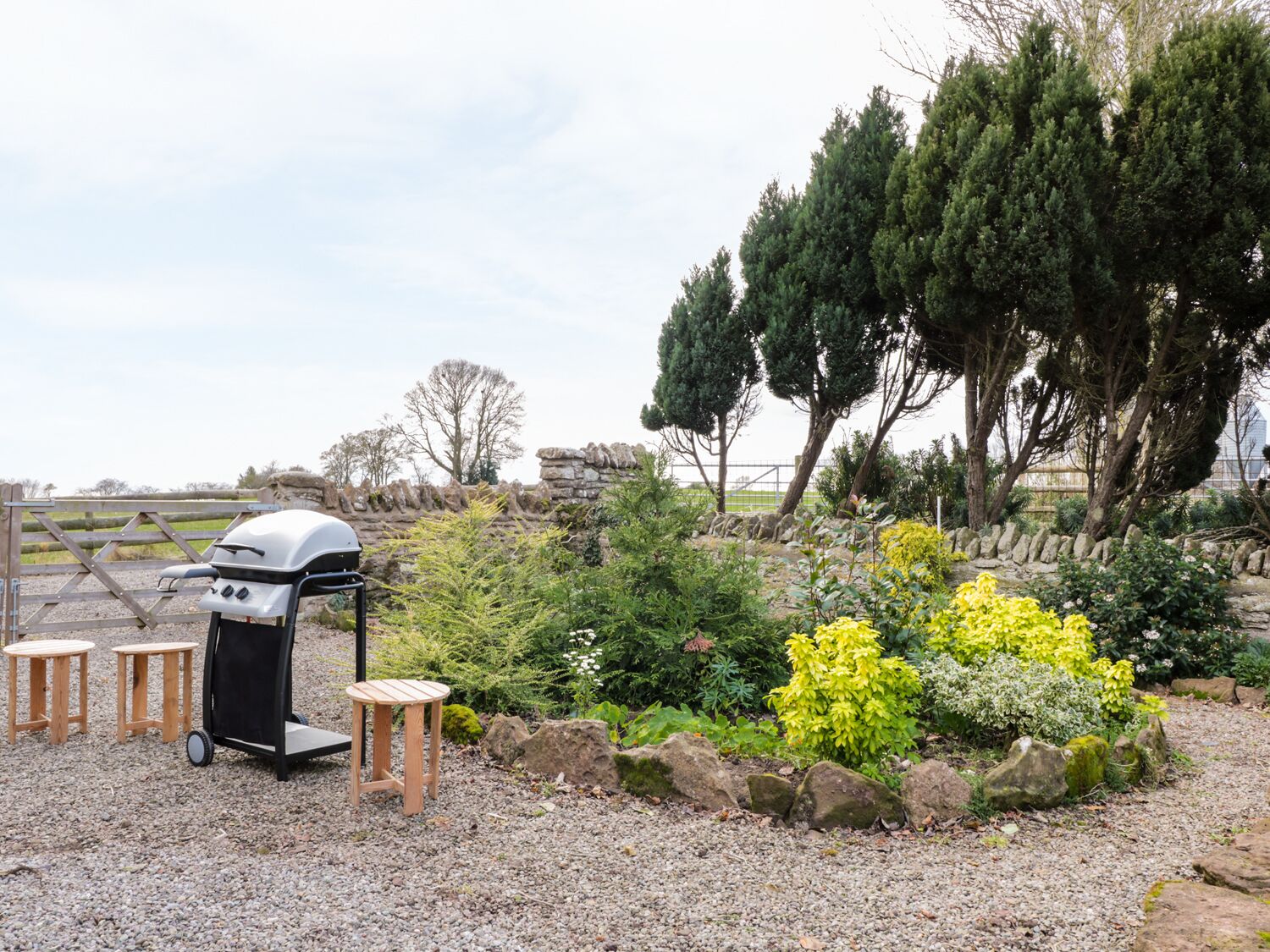 Un barbecue con sgabelli, immerso in un giardino ricco di piante e alberi.