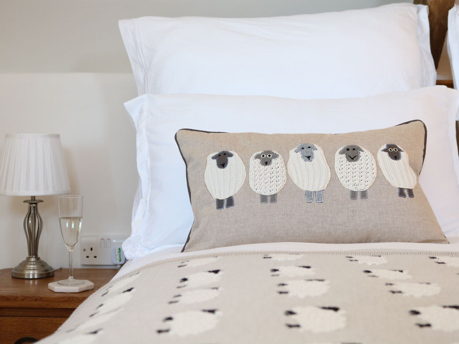 A bedroom with a bed, pillows, a bedside lamp, and a glass of water on a wooden nightstand.